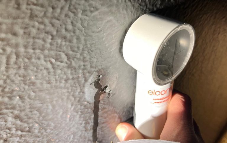 Hand hält ein Gerät gegen eine Wand, um eine Oberfläche zu untersuchen.