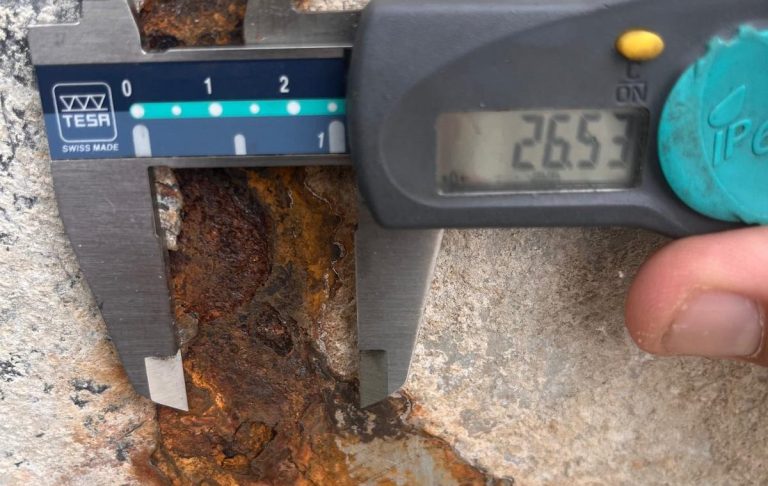 Messschieber zeigt eine Messung von 26,53 mm an einer rostigen Oberfläche.