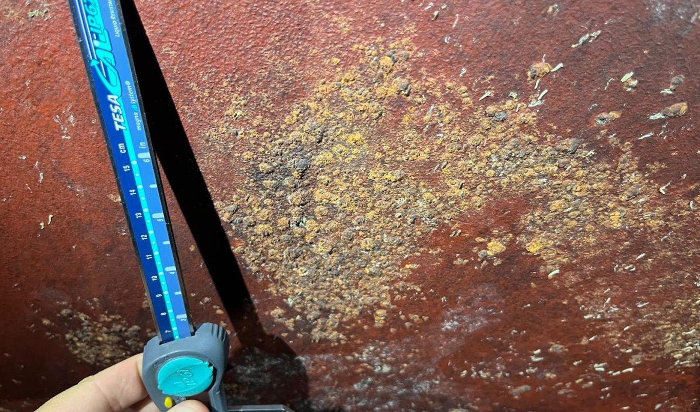 Brotrostige Oberfläche mit Rost und einem Messschieber zur Ermittlung der Korrosion.