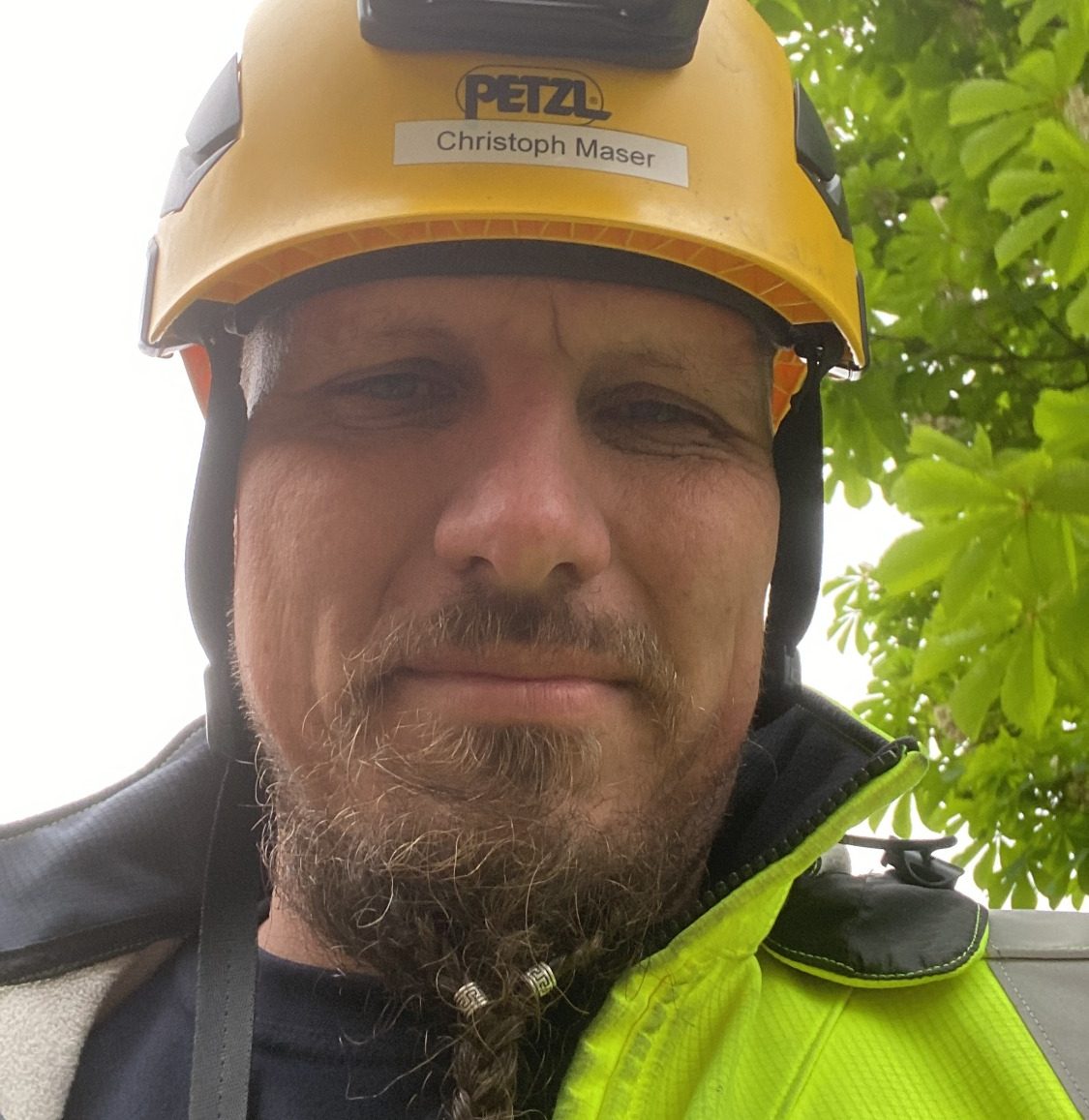 Ein Mann mit Helm und Sicherheitsjacke steht vor grünem Hintergrund.