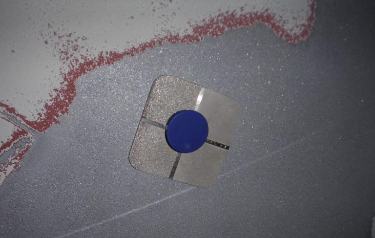 Ein transparenter Gegenstand mit einem blauen Zentrum, befestigt an einer grauen Fläche.